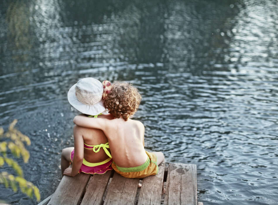 Boy,With,Arm,Around,Girl,,Sitting,On,Dock,In,Swimsuits